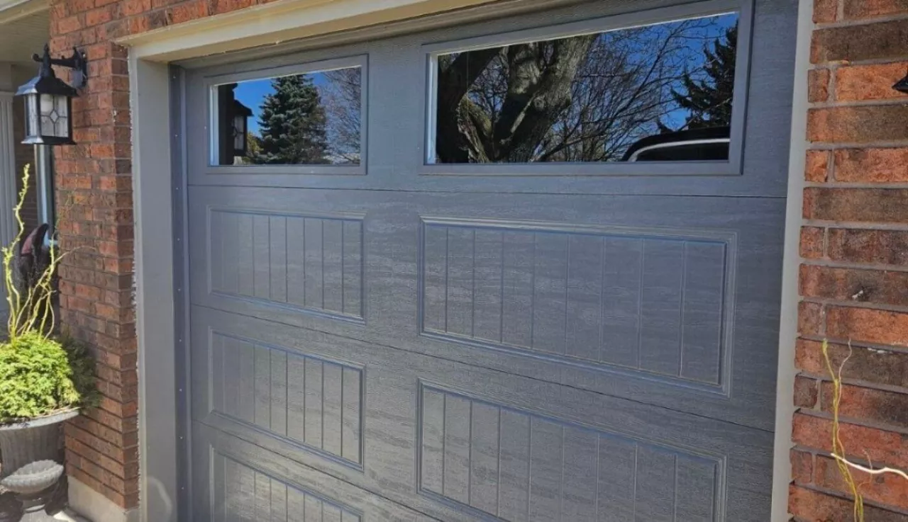 Garage door with windows and a potted plant beside it, adding greenery to the entrance.